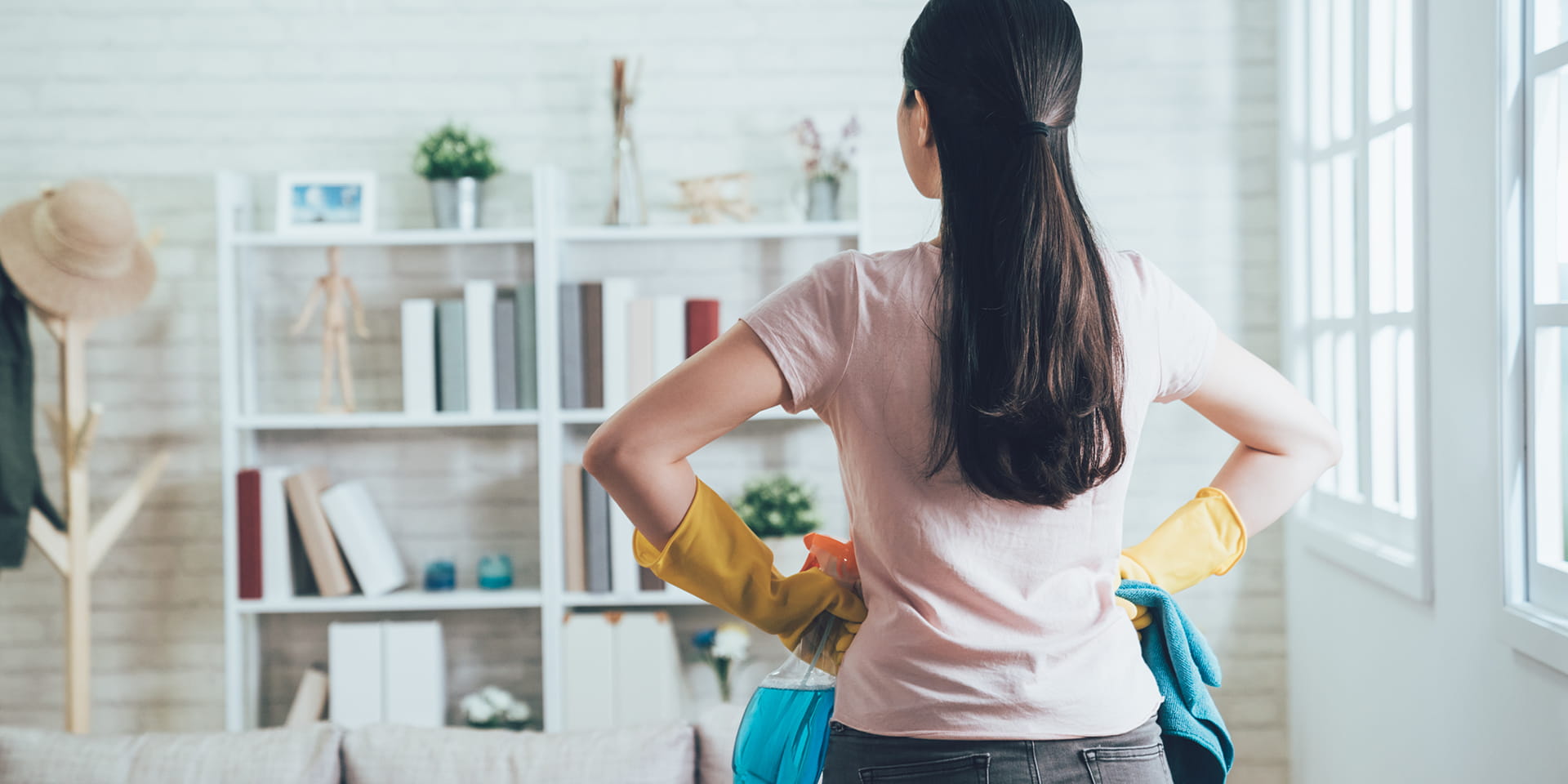 Woman with rubber gloves and hands on hips looks at her bookshelf