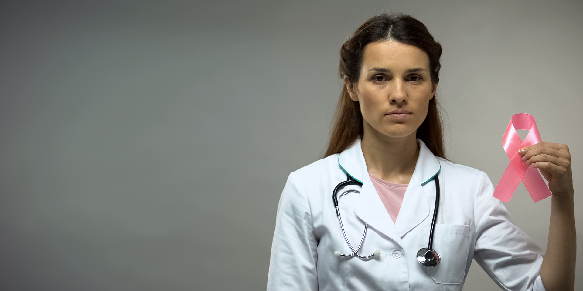 Female health provider holding a pink ribbon for breast cancer awareness.